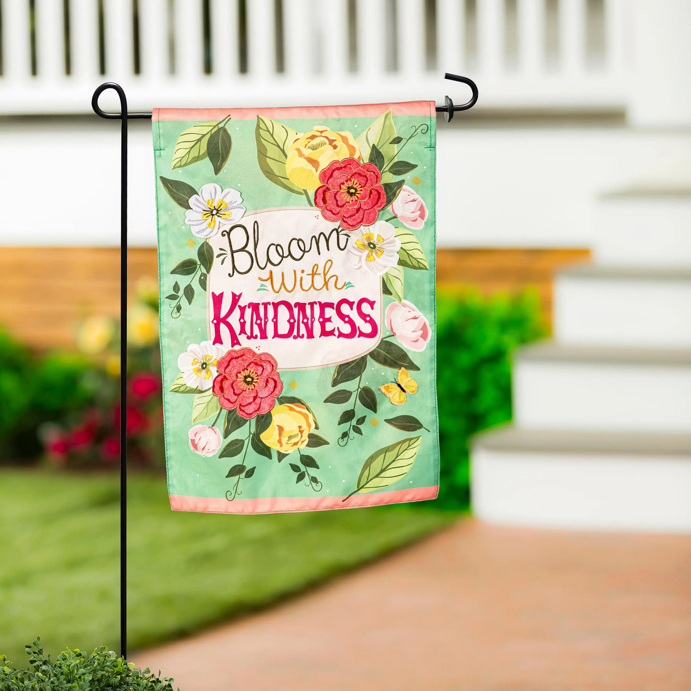 A vibrant mint green bloom with kindness applique garden flag with pink yellow white flowers and butterflies