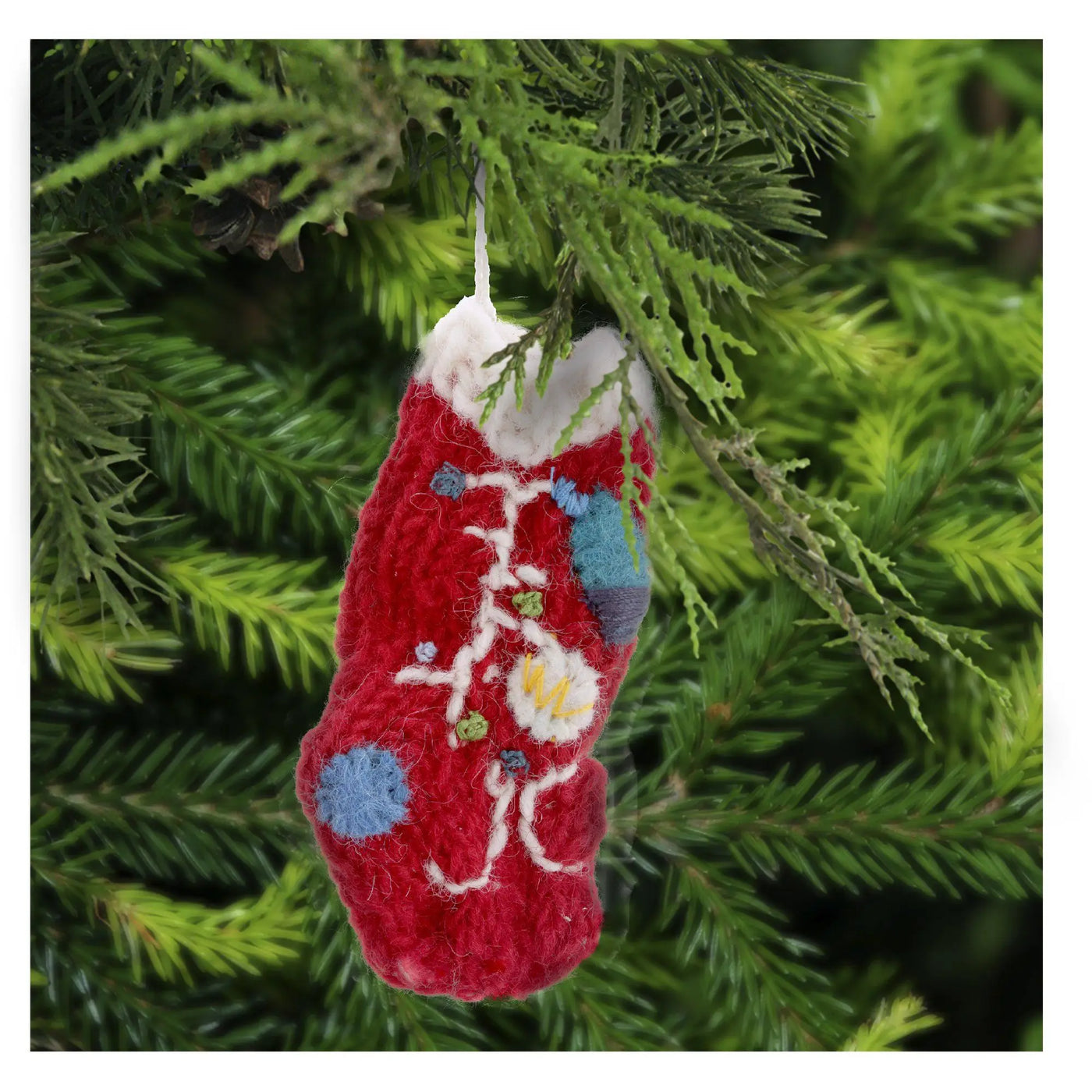 A red felt christmas lights stocking ornament with white blue and yellow embroidered details hanging on pine branch