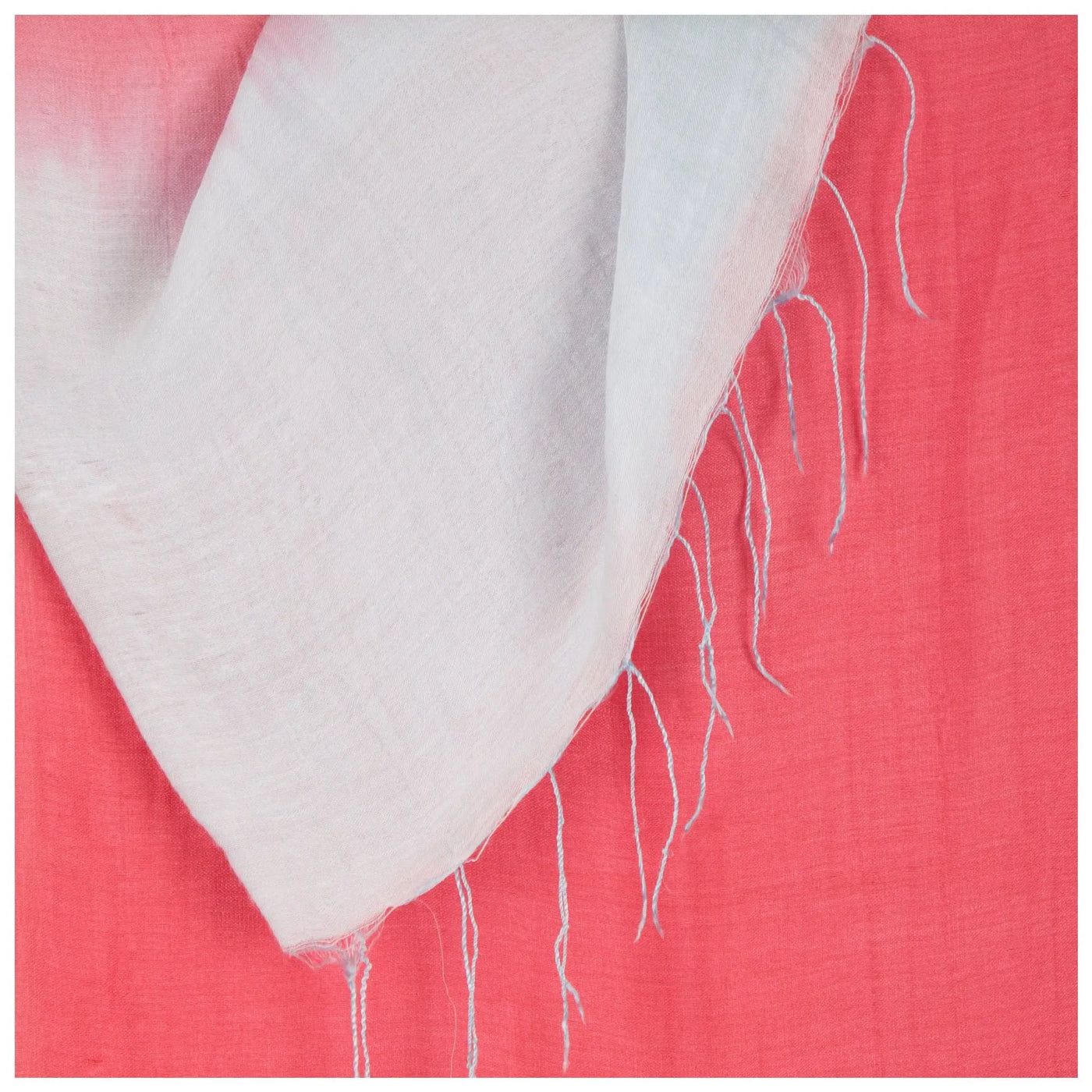 A soft off-white linen Color Connection scarf with delicate frayed edges on a vibrant coral background