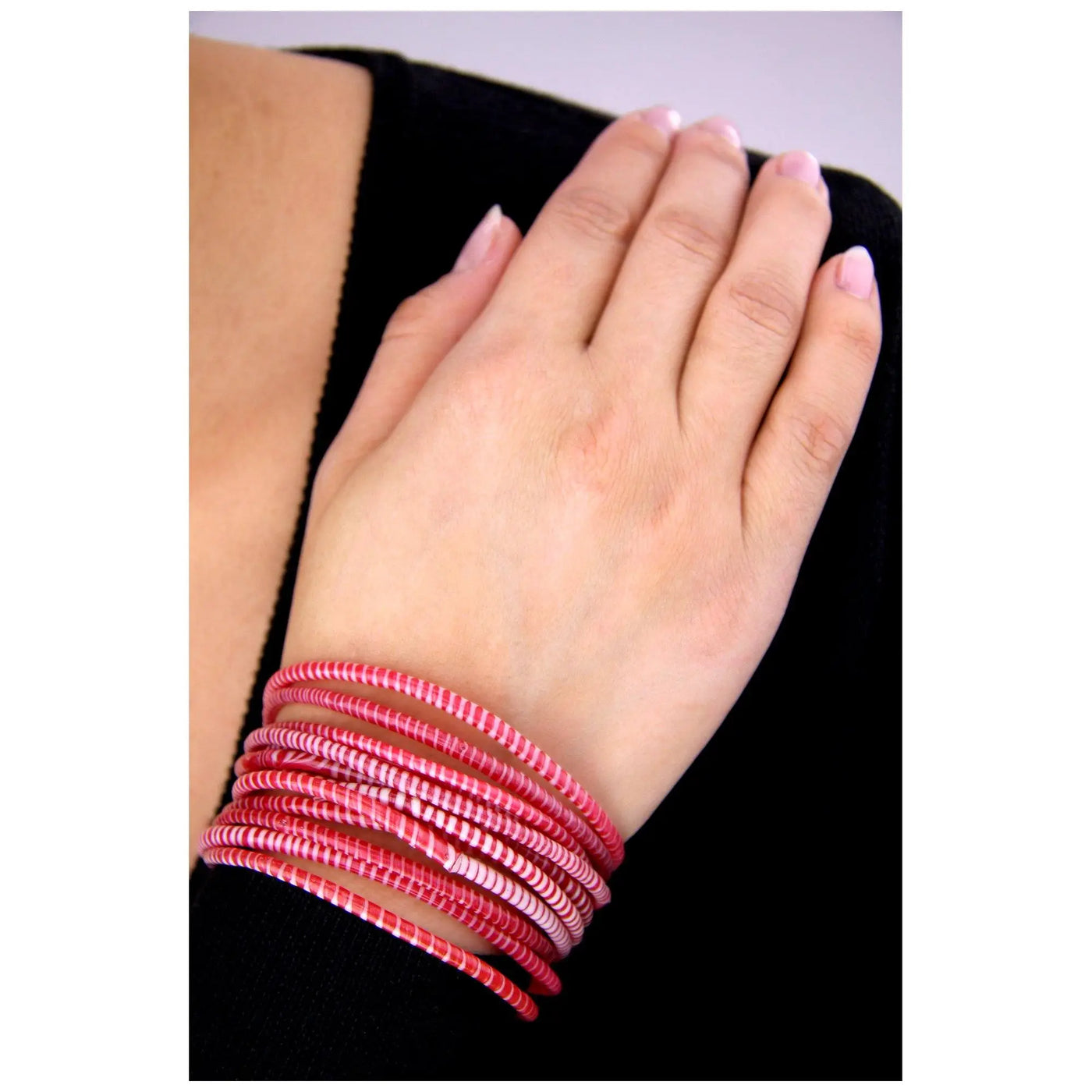 A stack of vibrant pink and white striped recycled bangles worn on wrist from colors of mali bracelet collection