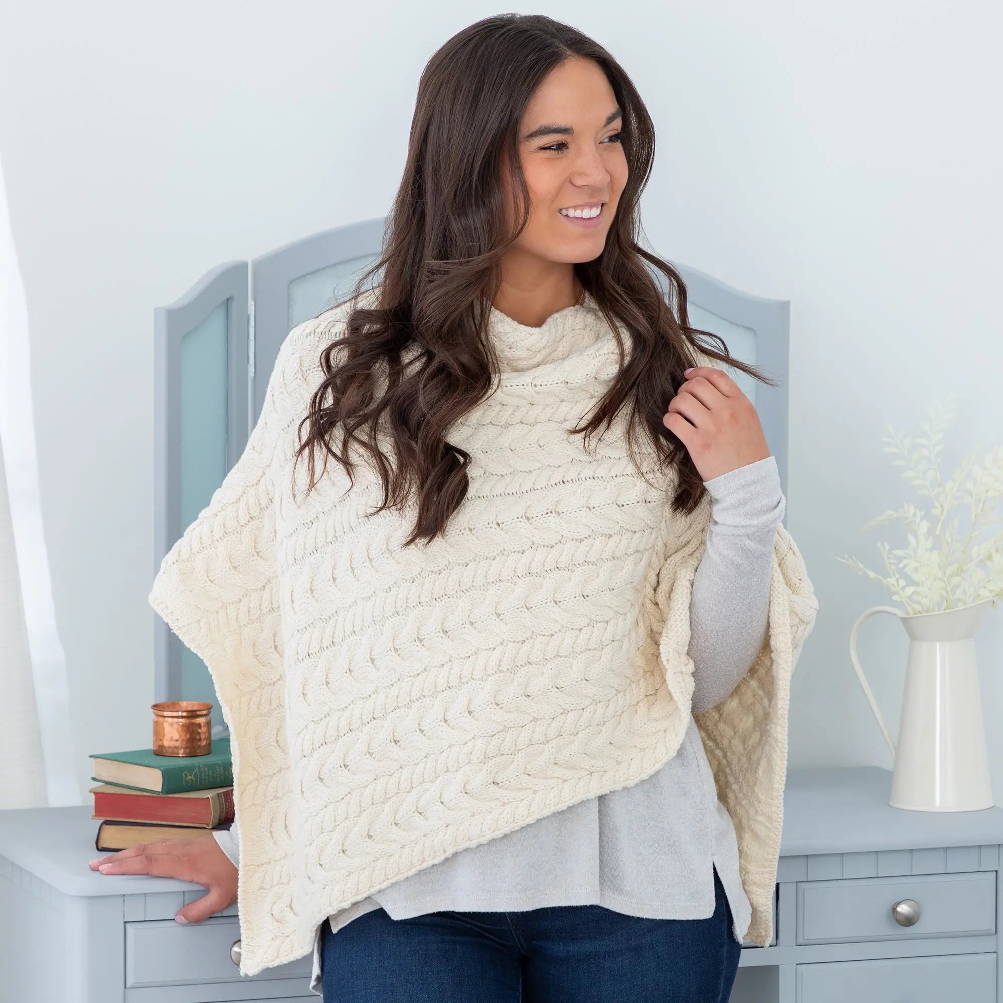 Cream-colored irish aran wool poncho with cable-knit texture, high neck, and wide sleeves