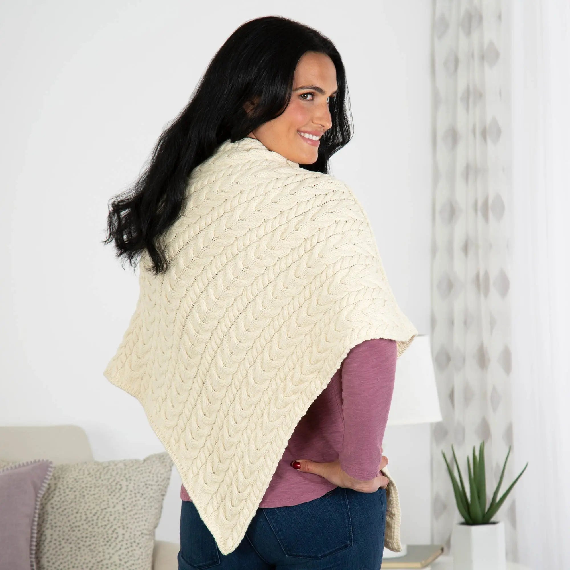 Cream-colored Irish Aran wool poncho with cable-knit texture draped over the model’s shoulders