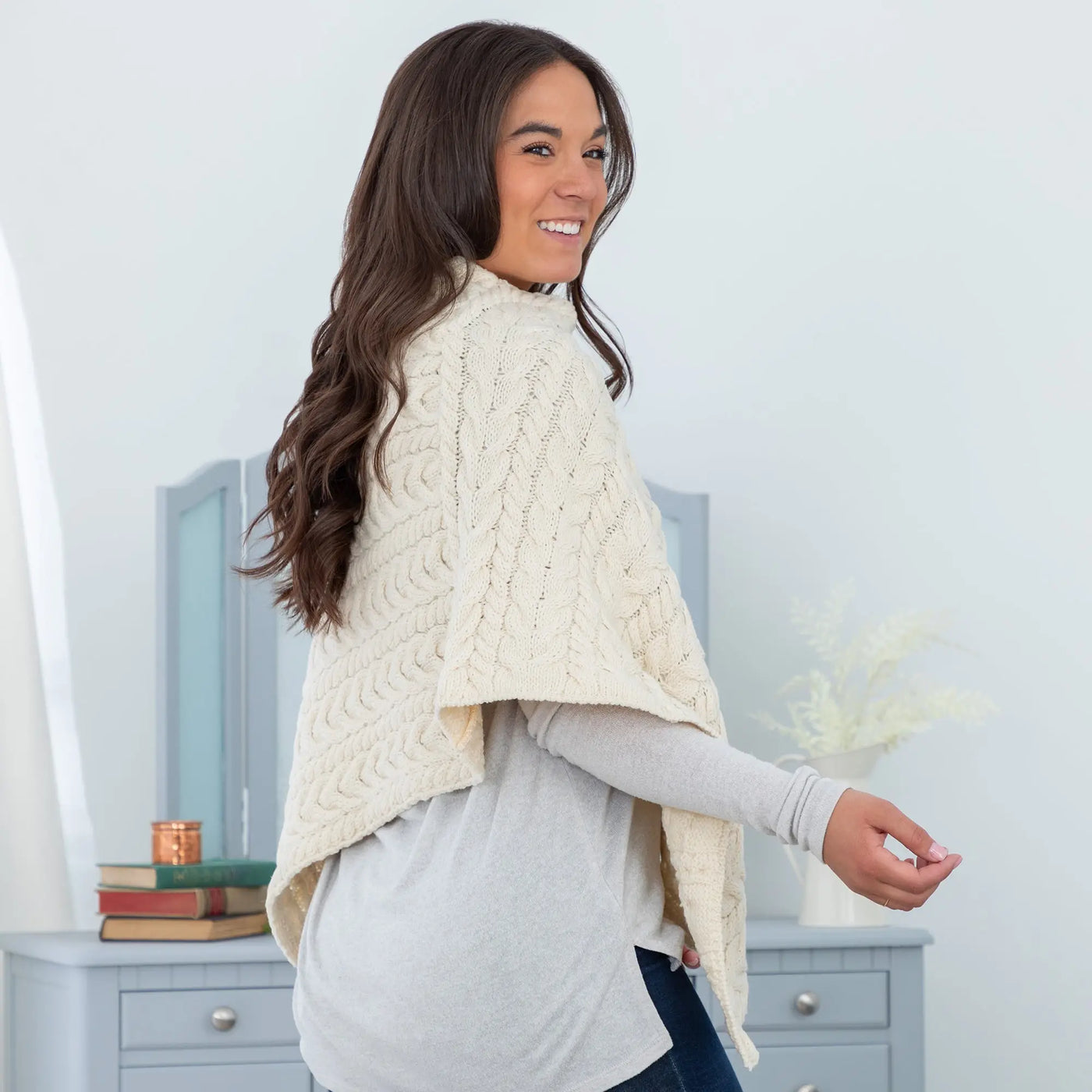 Cream-colored irish aran wool poncho with cable-knit texture high collar and open front for cozy wear