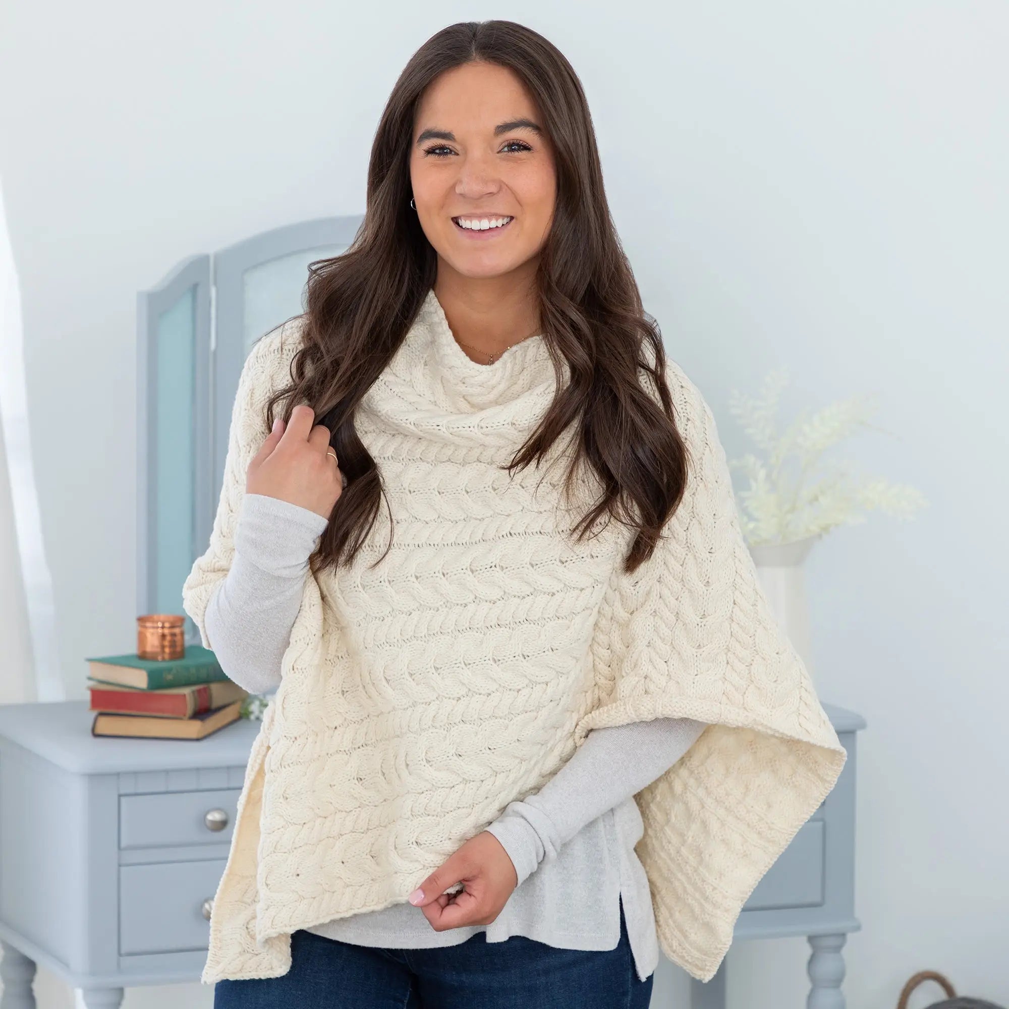 Cream-colored chunky-knit Irish aran wool poncho with cable knit pattern high cowl neck and draped sleeves