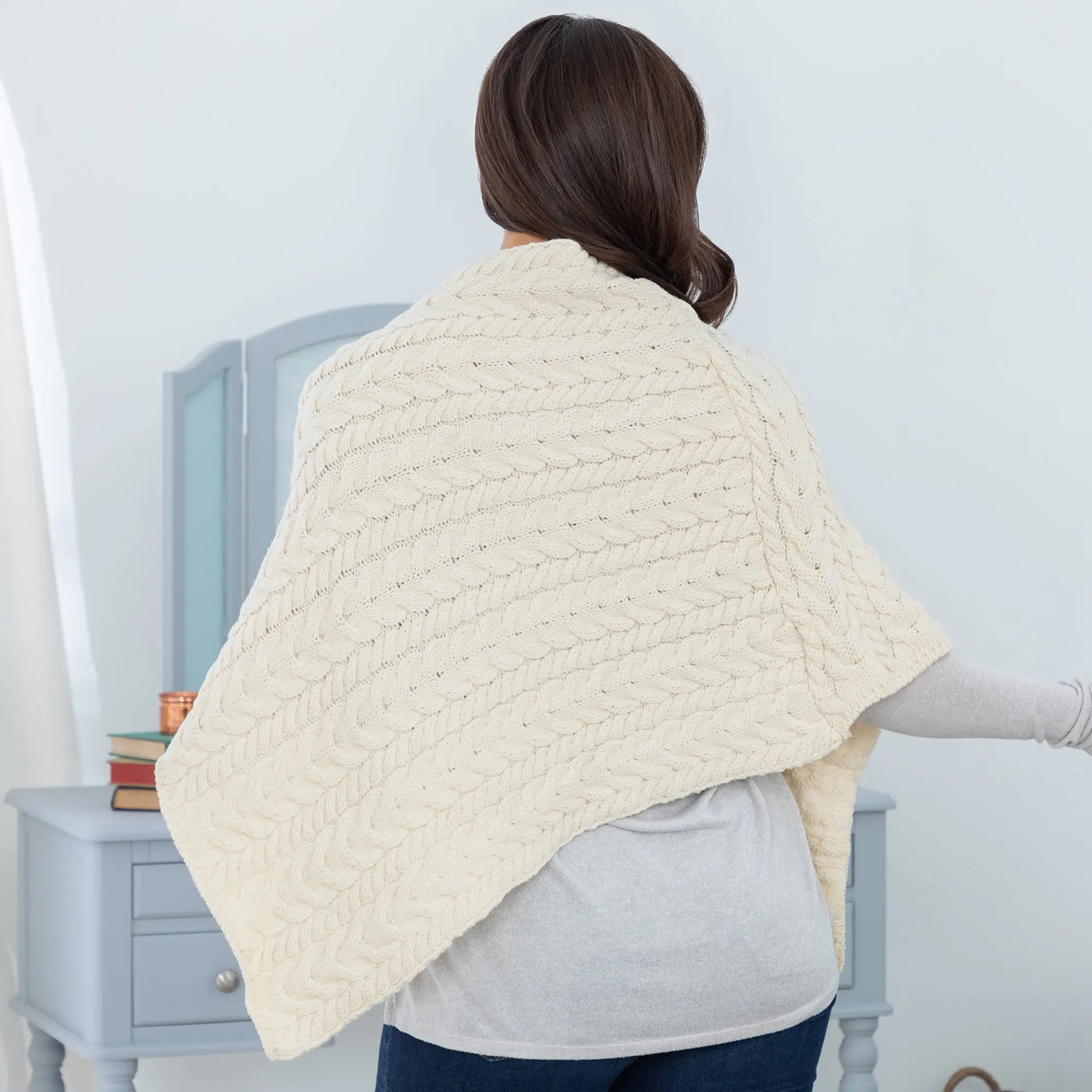 Cream-colored chunky-knit cable-patterned Irish Aran wool poncho draped over a womans shoulders