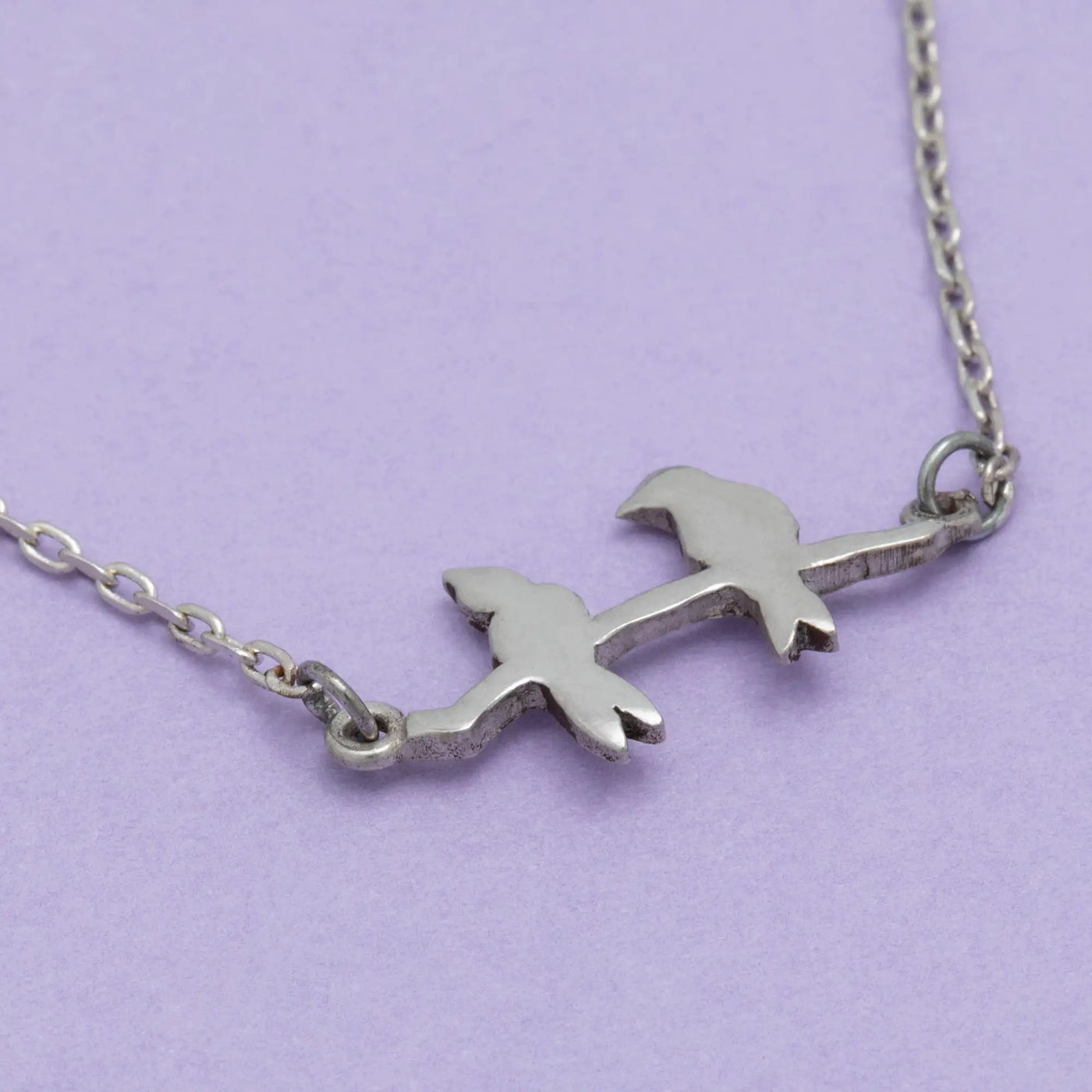 Silver sisterly love necklace with two stylized bird charms perched on a branch connected by an elegant chain