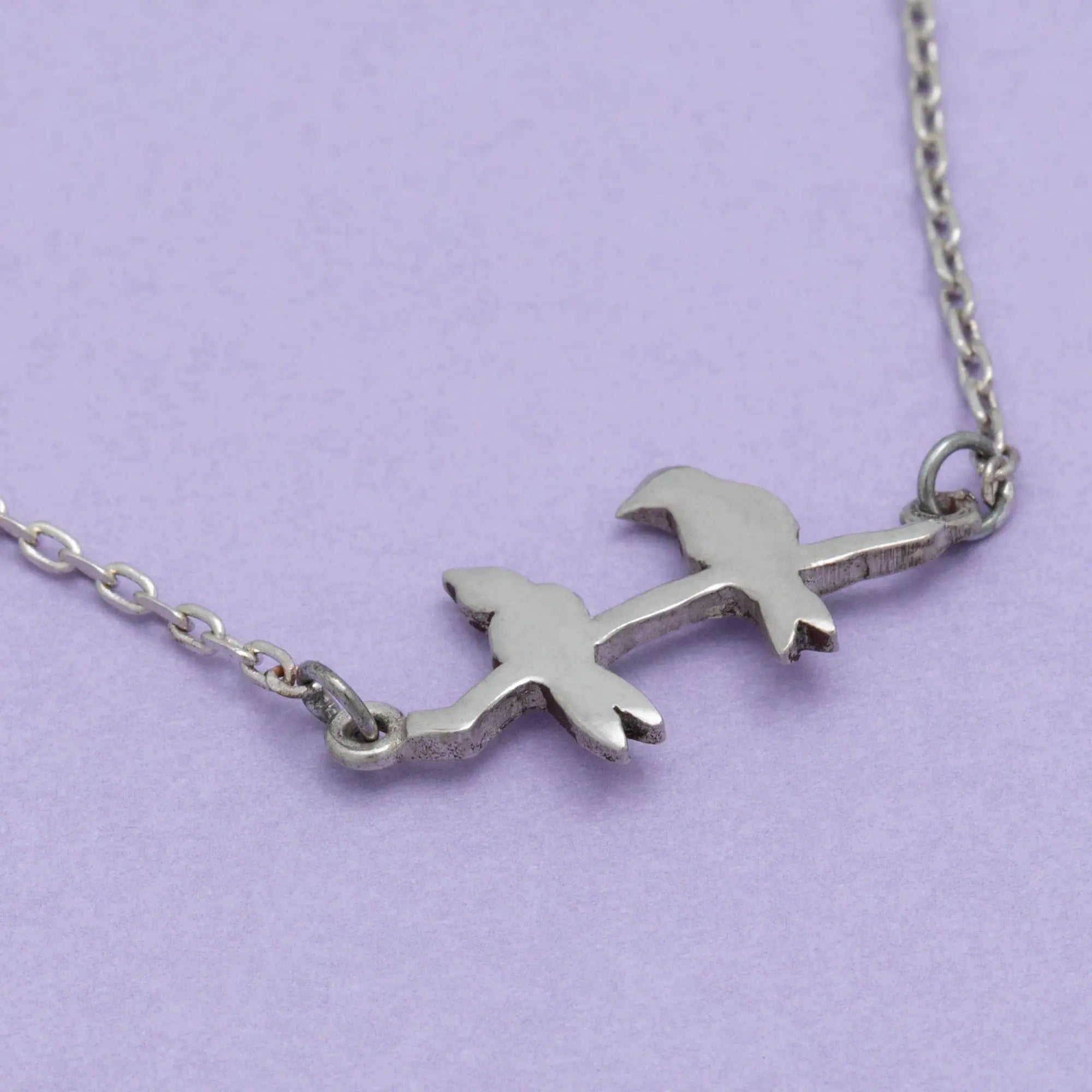Silver sisterly love necklace with two stylized bird charms perched on a branch connected by an elegant chain