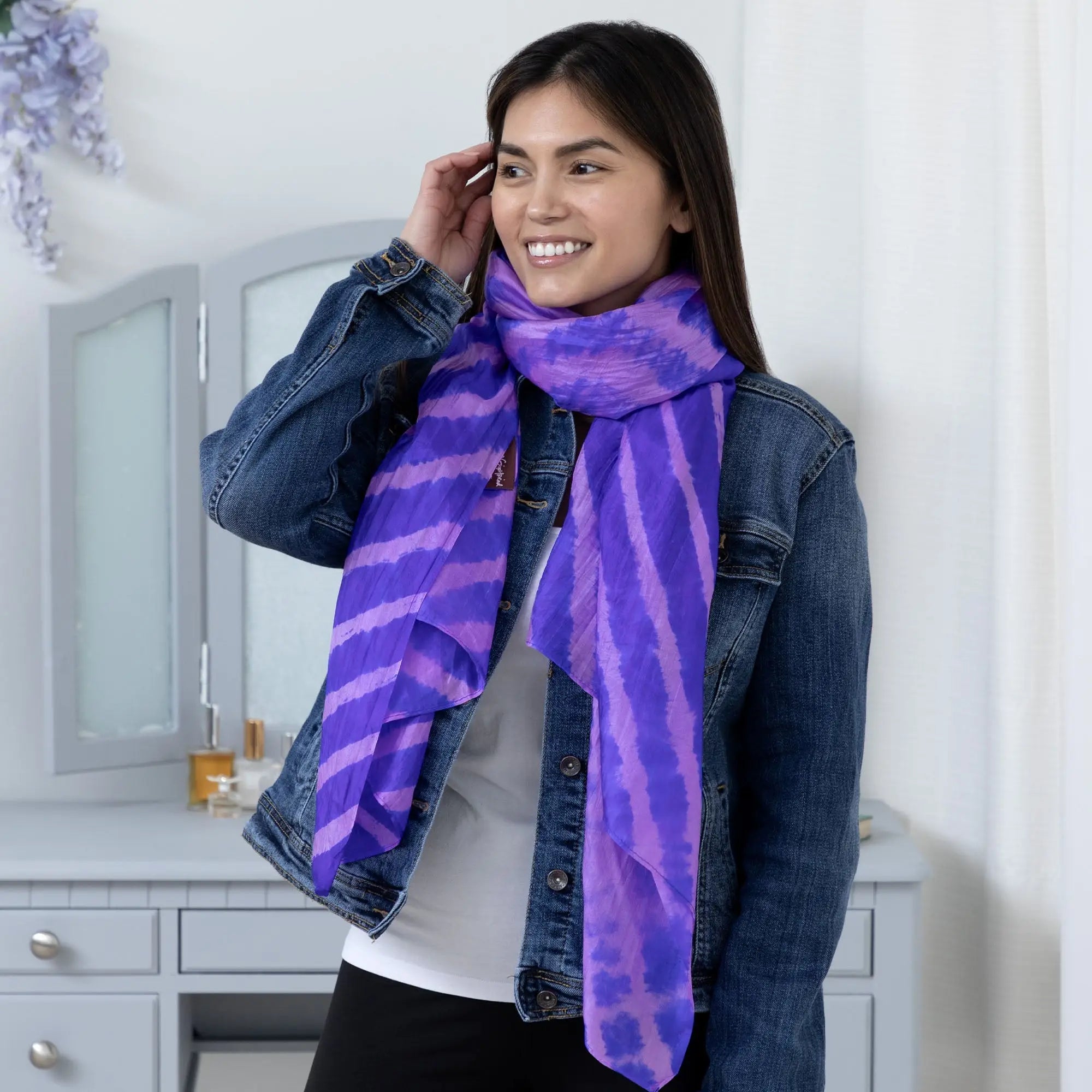 Tie-dye stripe silk scarf in vibrant purple and lavender with flowing ruffled edges worn around the neck