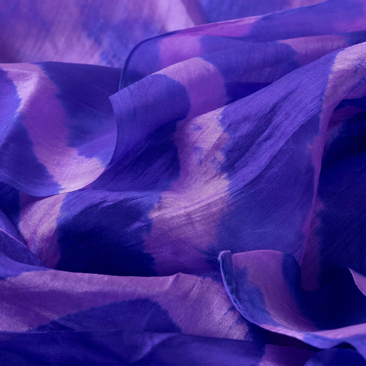 A flowing semi-transparent silk scarf with vibrant purple and deep blue tie-dye stripe pattern