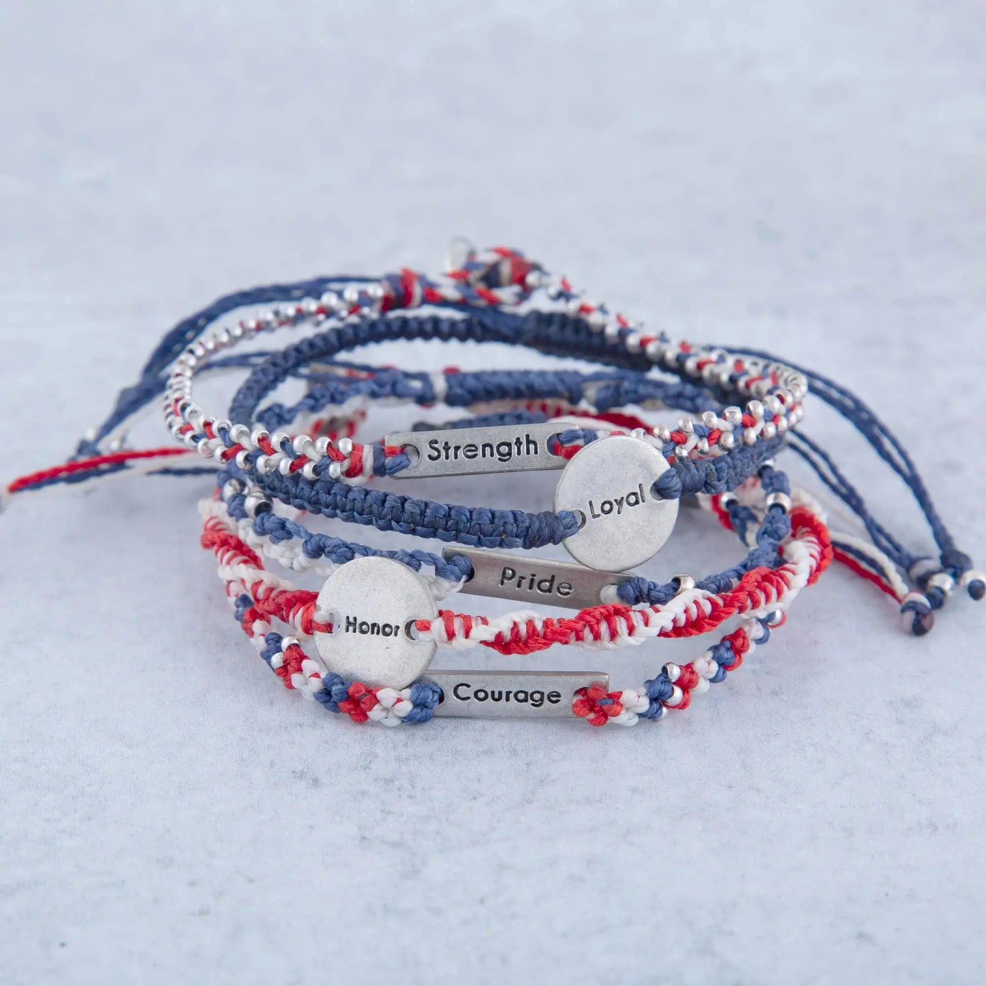 Red white and blue macrame friendship bracelets with engraved metal tags saying strength pride and courage wakami set of 5